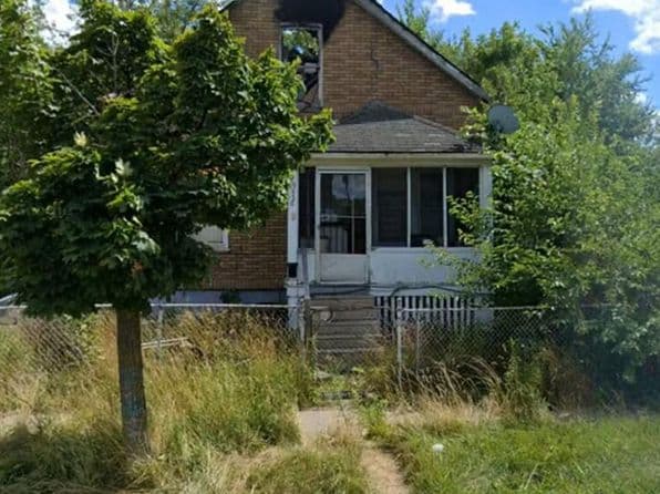 Brick house exterior with overgrown front yard and climbing vines