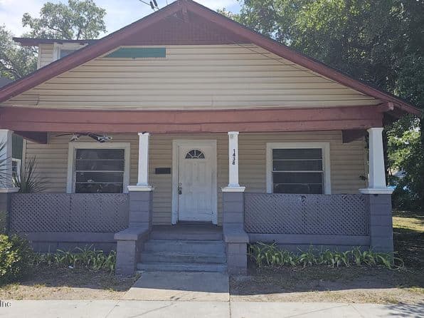 Tan residential property with red roof, white pillars, and garage doors