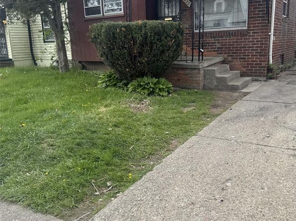 Exterior view of a 2 bed, 1 bath home with a lawn and steps.
