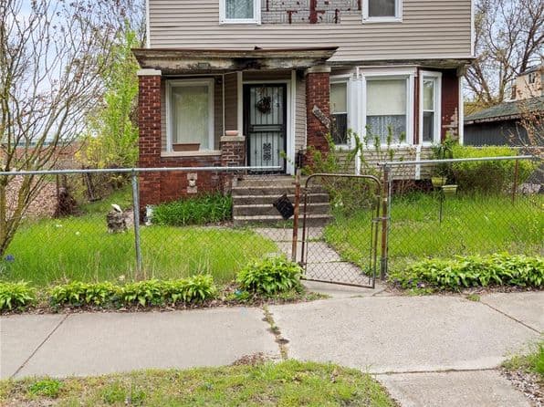 A two-story home with a fenced yard and front steps, featuring greenery and a welcoming entry.